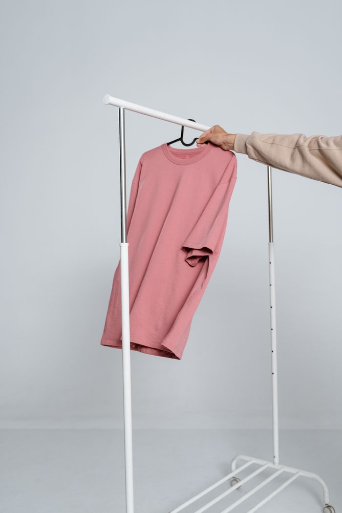 Pink shirt hanging on a white clothing rack in a minimalist setting.